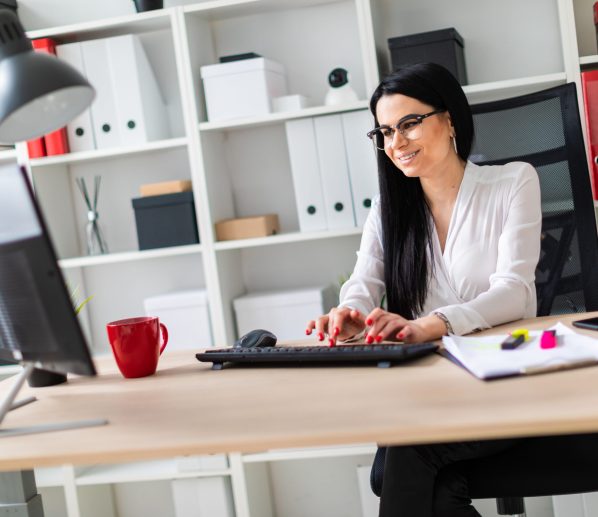 A young girl with glasses, wearing a white blouse and black trousers, works in the office. The girl has long straight black hair. photo with depth of field